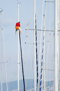 Man working attached on the top af a sailboat mast