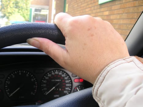 hand on a steering wheel of a car as the person drives along the road