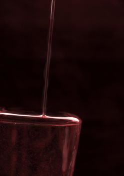 overflowing glass of red red wine against a dark background