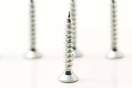 one screw standing in front of three on white background