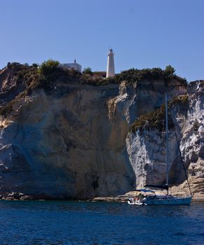 Lighthouse on steep mountain and sail yacht near Ponza island (Italy).