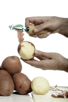 Closeup view of a male hand peeling an organic red potato, isolated against a white background.