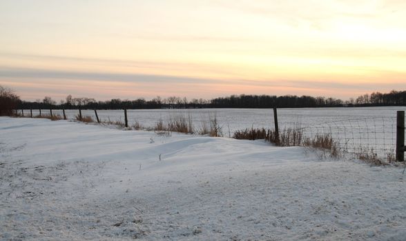 A snowy field with a fence set against the evening sky