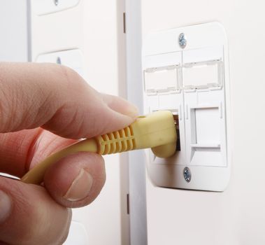 Cable guy inserting a network cable into the slot on the wall