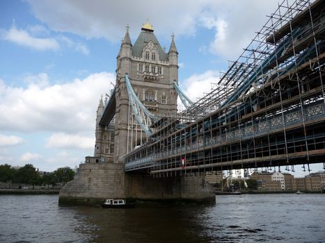 A view of the historic Tower Bridge partly covered in scaffolding, which is located over the River Thames in London.
.
