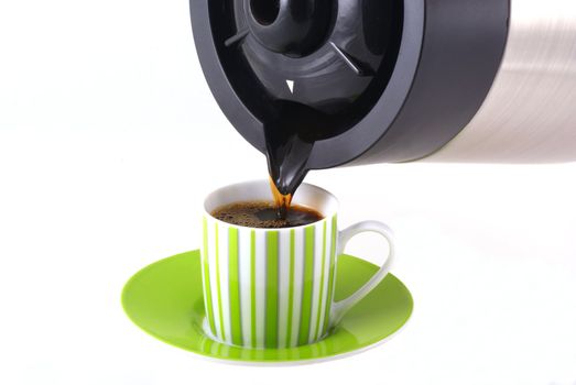 Coffee being poured out of a pot into a cup with saucer.          