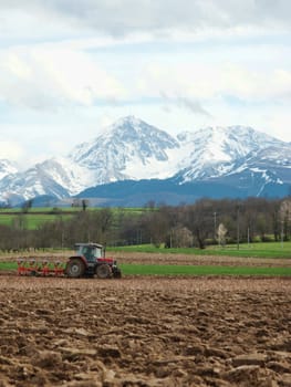 Scenic  landscape with a farmer plowing a field with French Pyrenees mountains in the background