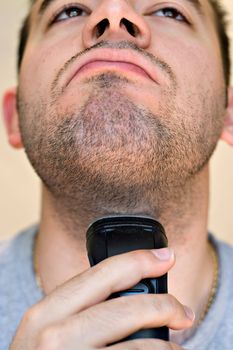 A closeup of a young man shaving his beard off with an electric shaver.