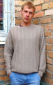 Young stylish man with blonde hair stand near brick wall.