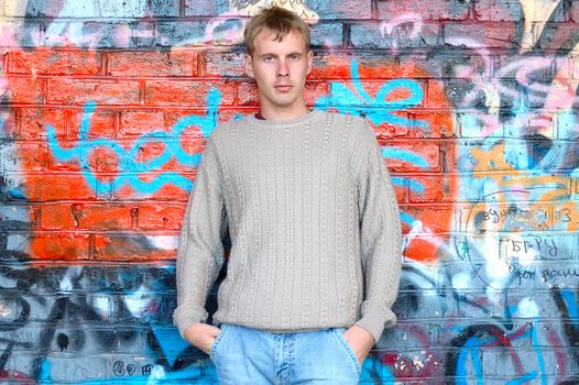 Young stylish man with blonde hair stand near graffiti brick wall.