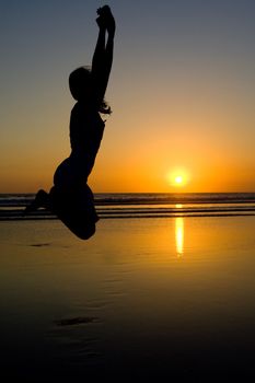 Woman jumping on the beach at sunset.