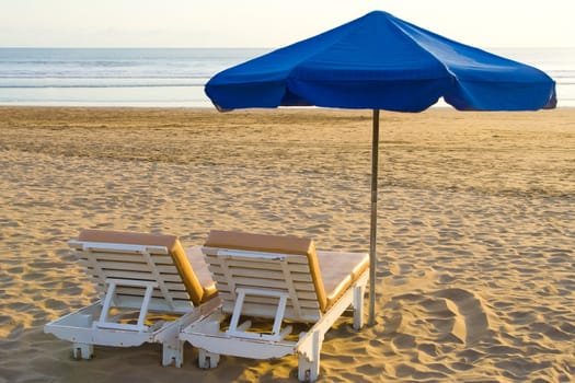 Sun, umbrella and chairs on sandy beach.