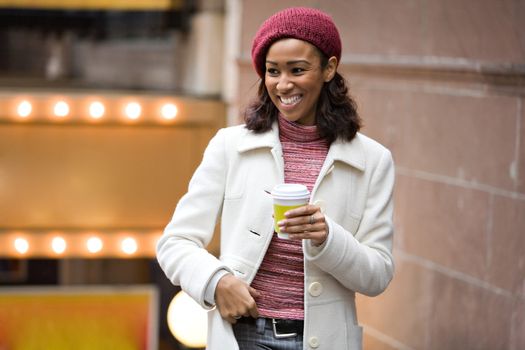 An African American business woman is walking through the city holding a cup of coffee tea or cappuccino.
