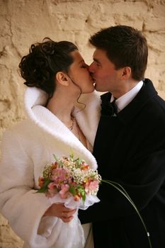 The groom and the bride kiss on a background of a wall
