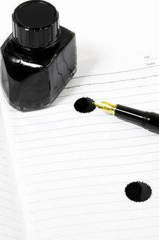 classic black fountain pen on open notebook with ink bottle with stain on page