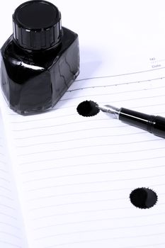 classic black fountain pen on open notebook with ink bottle with stain on page,blue filter