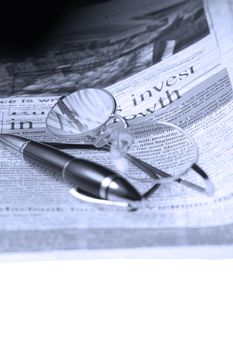 pen and glassesand newspaper over white glass table