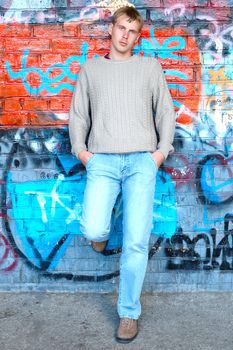 Young stylish man with blonde hair stand near graffiti brick wall.