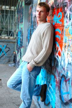 Young stylish man with blonde hair stand near graffiti brick wall.