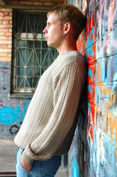 Young stylish man with blonde hair stand near graffiti brick wall.