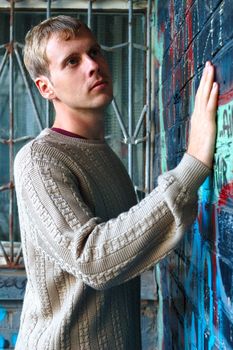 Young stylish man with blonde hair stand near graffiti brick wall.