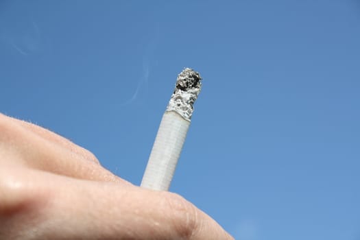 Focus on cigarette in human fingers on a blue sky background