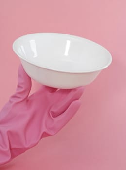 hand with glove on holding a white bowl, pink background