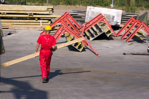 Construction worker in red work wear carrying wooden plank
