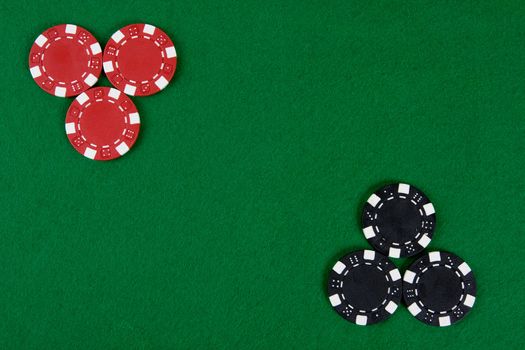 Two kinds of poker chips in two corners of a green poker table. Top view.