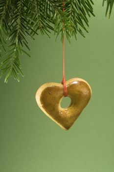 Heart shaped gingerbread cookie hanging by ribbon and isolated against green paper