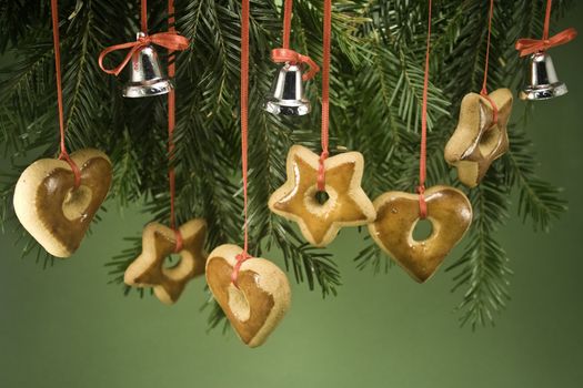 Gingerbread ornaments and tiny bells handing by ribbon under a fir branch and isolated on green paper