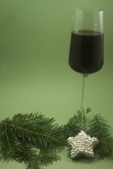 A glass of red wine and single star cookie with fir branch isolated on green paper