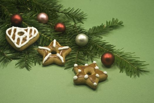 Three cookies and five shiny balls on fir branch isolated on green paper
