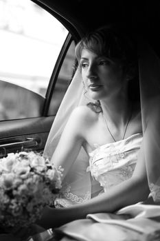 The beautiful bride with a bouquet in the automobile