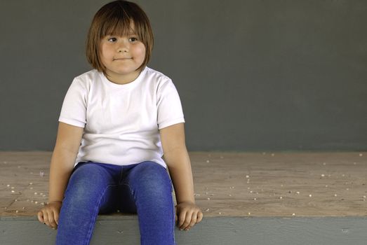 A young five year old girl is sitting on a stage waiting for something.