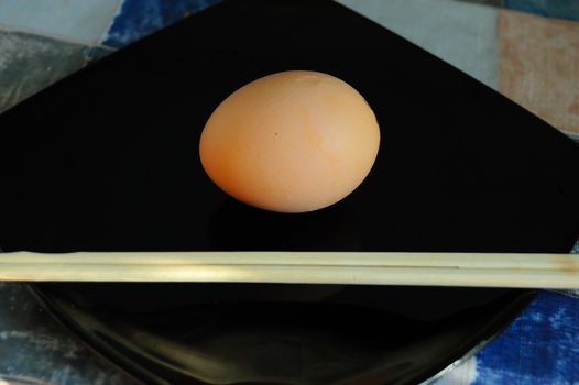 irony healthy diet concept - raw egg on black plate and chopsticks