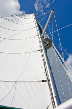 Mast and sails with radar and GPS standing tall with deep blue sky and white clouds