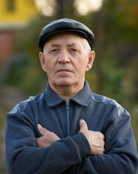 Portrait of the elderly man in a cap against the nature
