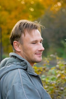 The smiling young man in a grey jacket against the autumn nature