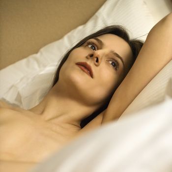Nude Caucasian mid-adult woman relaxing in bed.