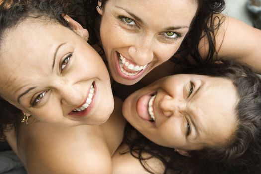 Three nude brunette Caucasian mid-adult women embracing each other looking up at viewer and smiling.