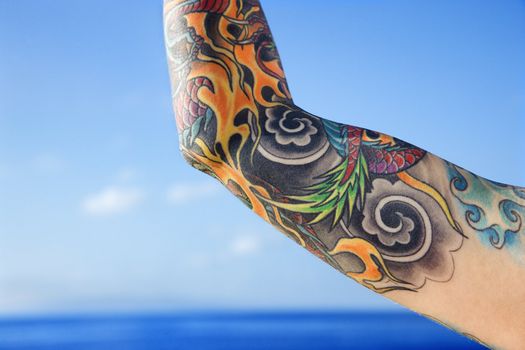 Close up of tattooed woman's arm with Pacific Ocean in background in Maui, Hawaii, USA.