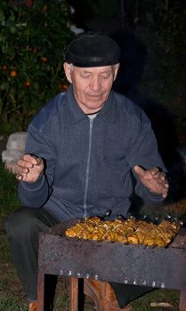 The elderly man prepares a shish kebab on picnic