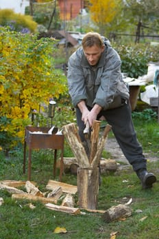 The young man pricks fire wood an axe in the court yard. Autumn, outdoor