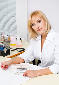 beautiful blond female manicurist portrait at work. interior of nail salon.