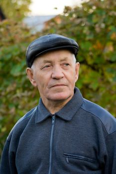 Portrait of the elderly man in a cap against the nature
