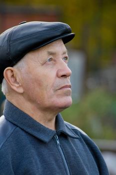 Portrait of the elderly man in a cap against the nature