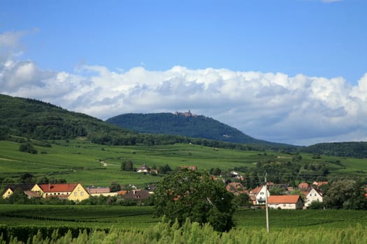 Haut-Koenigsbourg castle on peak of Vosges. Vineyards and small village in the valley. Alsace, France.