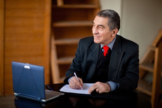 Senior businessman writing and working with document indoors