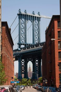 The Manhattan Bridge as seen from Brooklyn with the Empire State building underneath its arc. The street shows historic brownstone buildings used to be warehouses.